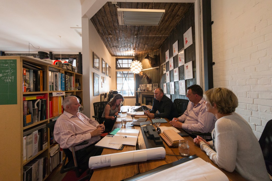 Architect Charlie Nott discusses materials with clients around a table in his studio.