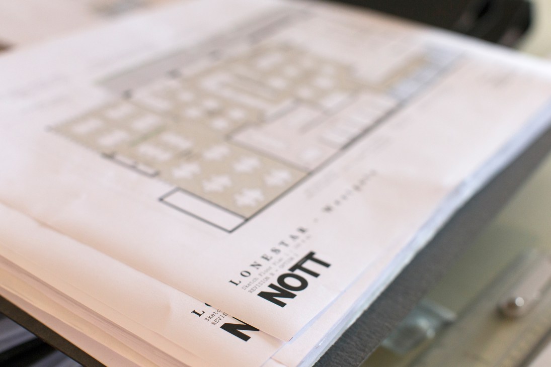 Architectural drawings and plans for a hospitality project by Nott Architects spread on a table.