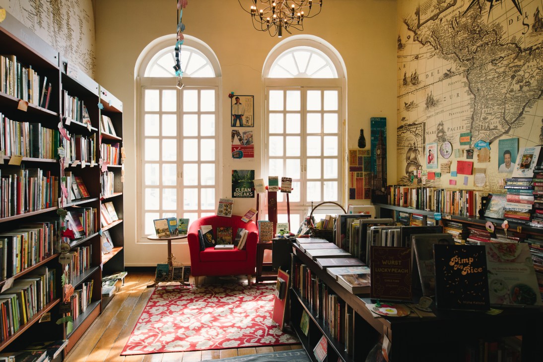 Interior of Littered with Books bookshop in Duxton Hill featuring shelves, a red armchair, and tall arched windows.