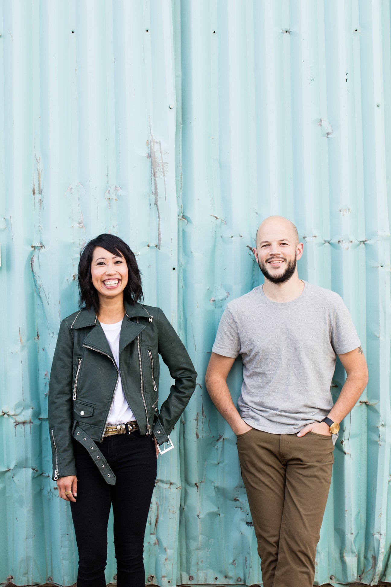 Amor and Chris Provins of Hunt Amor standing together and smiling in front of weathered turquoise metal siding