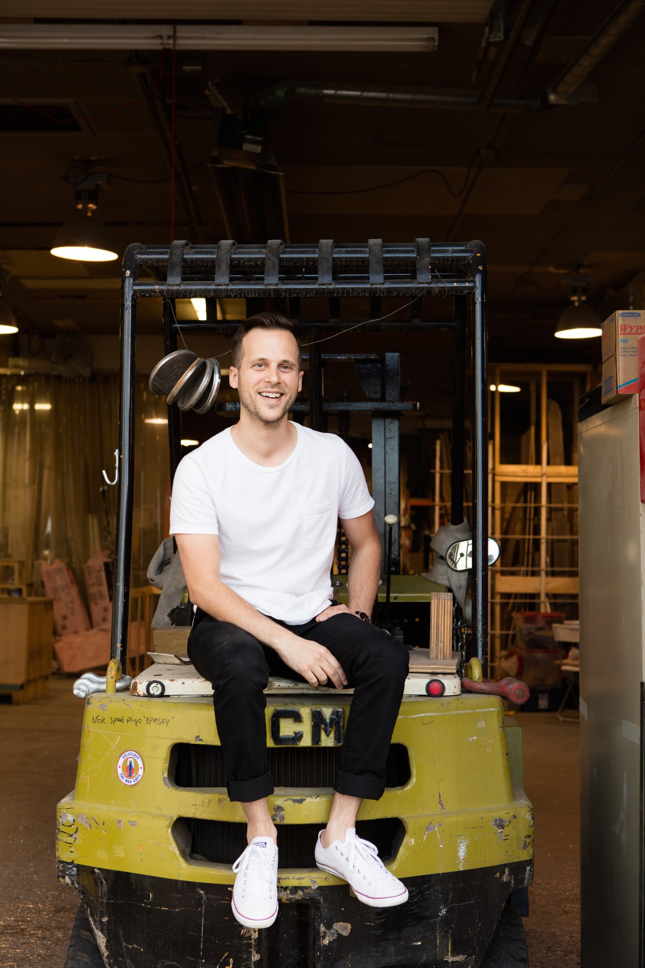Jordan Tomnuk sitting on yellow forklift in workshop space