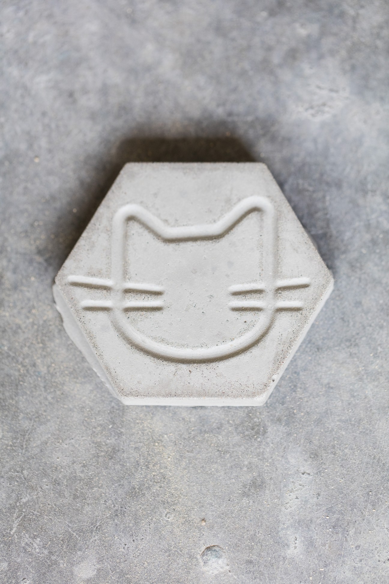 Hexagonal white concrete tile with embossed cat face design featuring ears, whiskers and smile