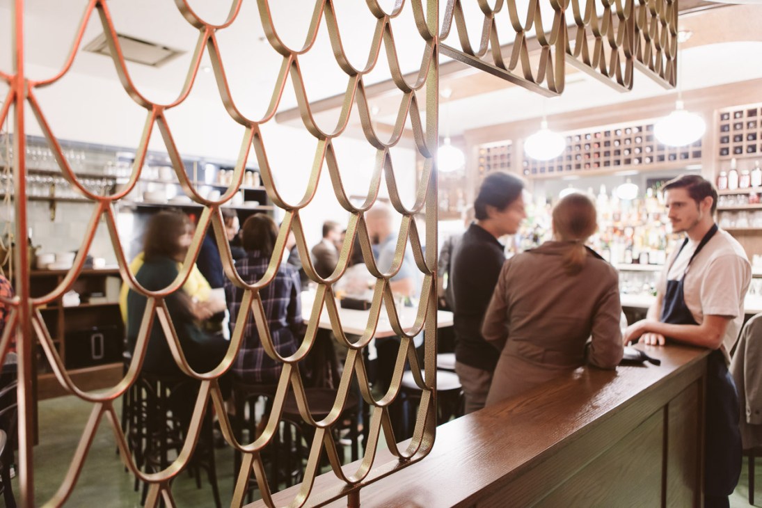 Decorative metal chain-link screen overlooking blurred figures in Bar Clementine restaurant interior