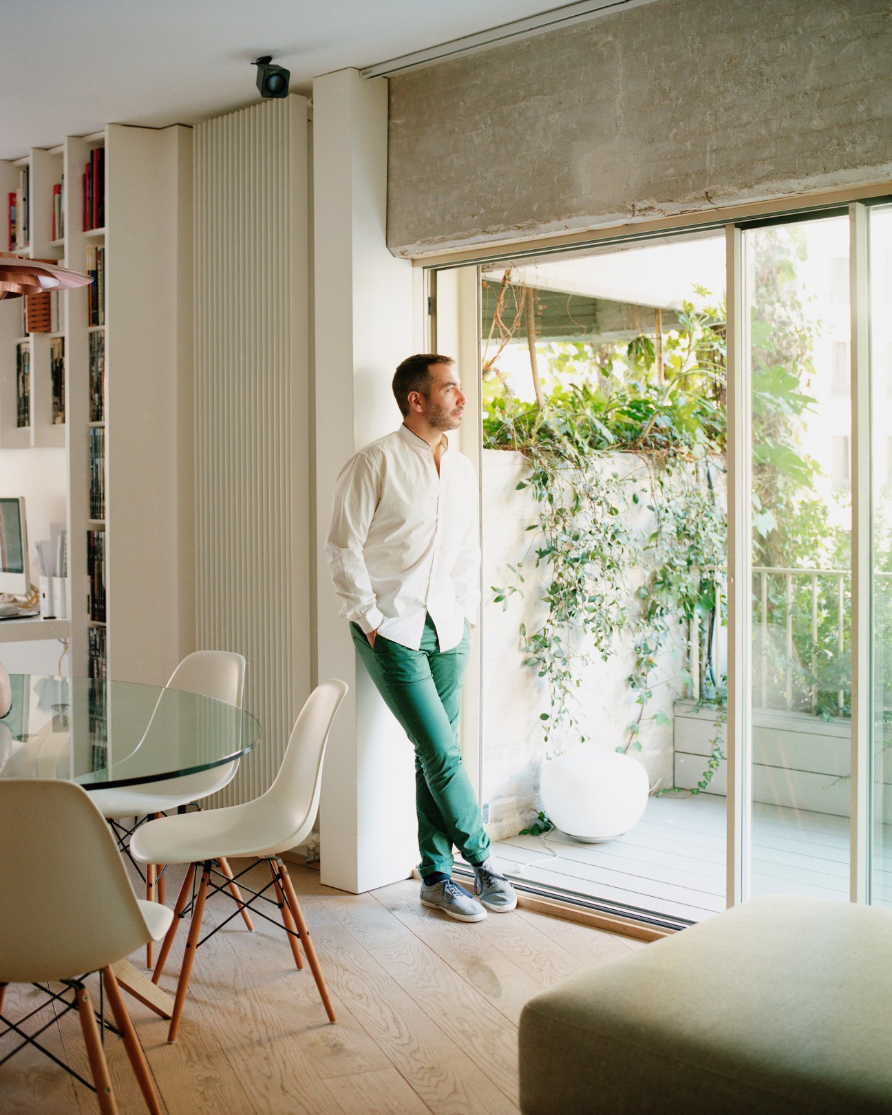 Architect Angel Cazorla stands in his modern home office beside large glass doors opening onto a verdant balcony with climbing plants.