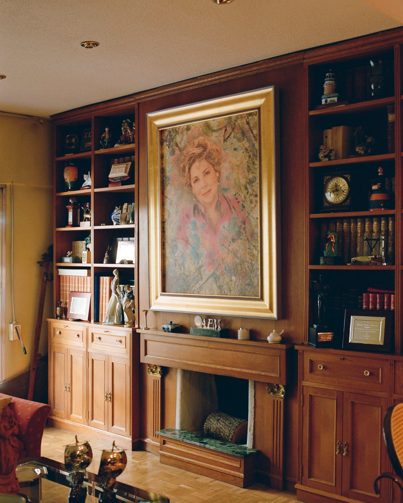 Portrait of Paloma Gómez Borrero hangs in a gold frame above a fireplace with wooden shelving.