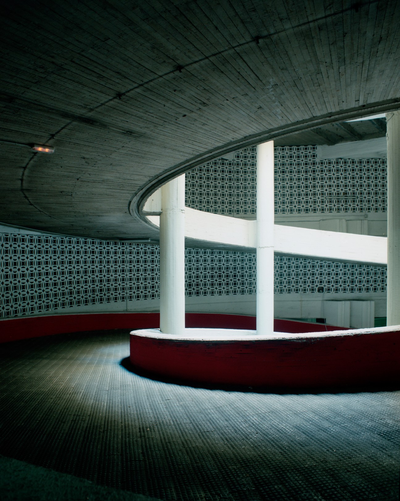 Curved ramp in a modernist subterranean carpark with geometric patterned walls and red circular seating.
