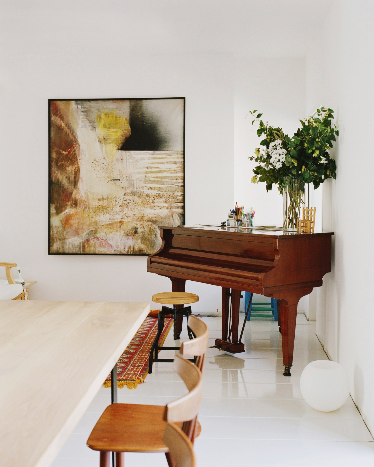 Modern apartment interior with piano, abstract artwork, fresh flowers and wooden furniture.