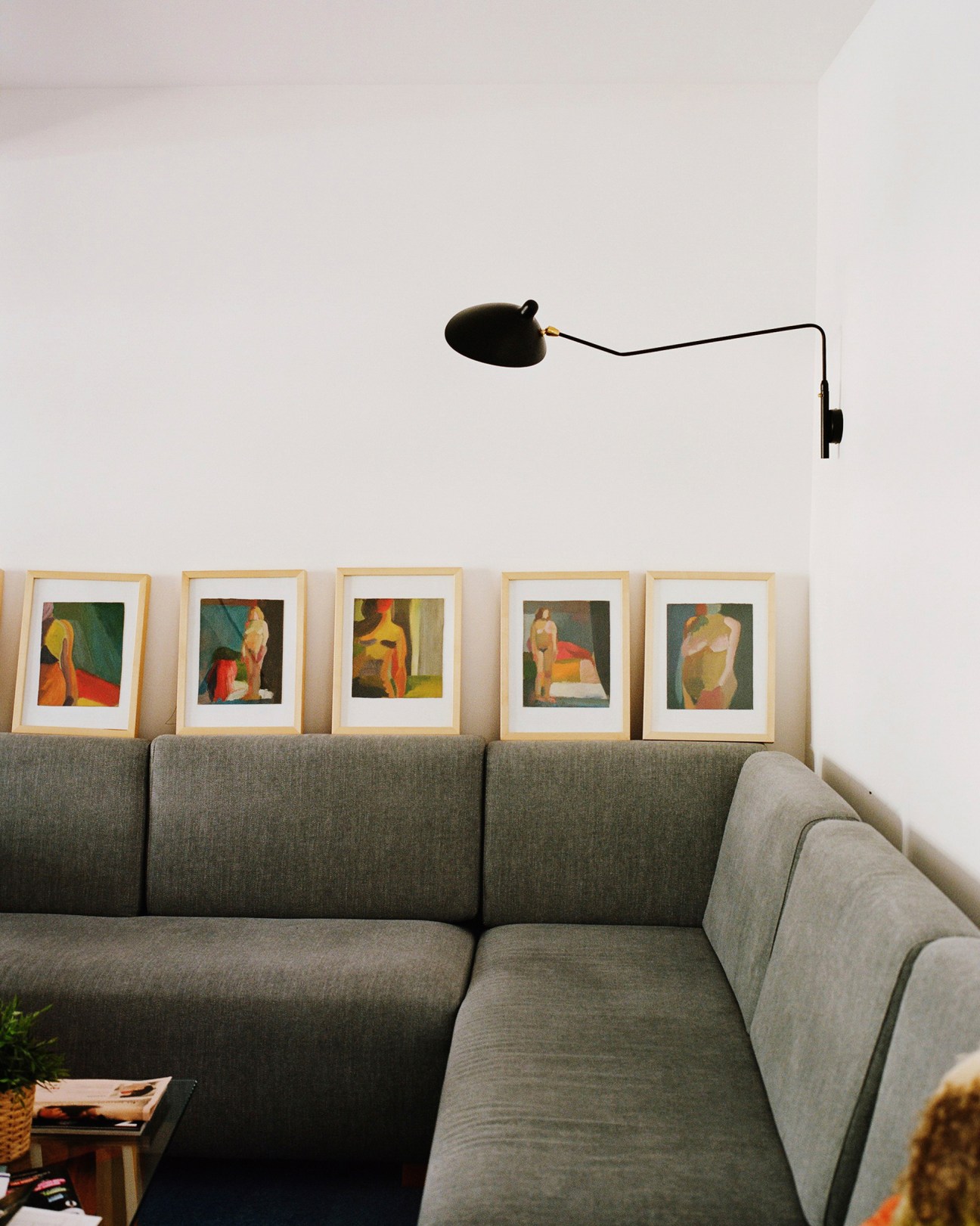 Gray sectional sofa with framed artworks displayed on wall above and black articulated wall lamp.