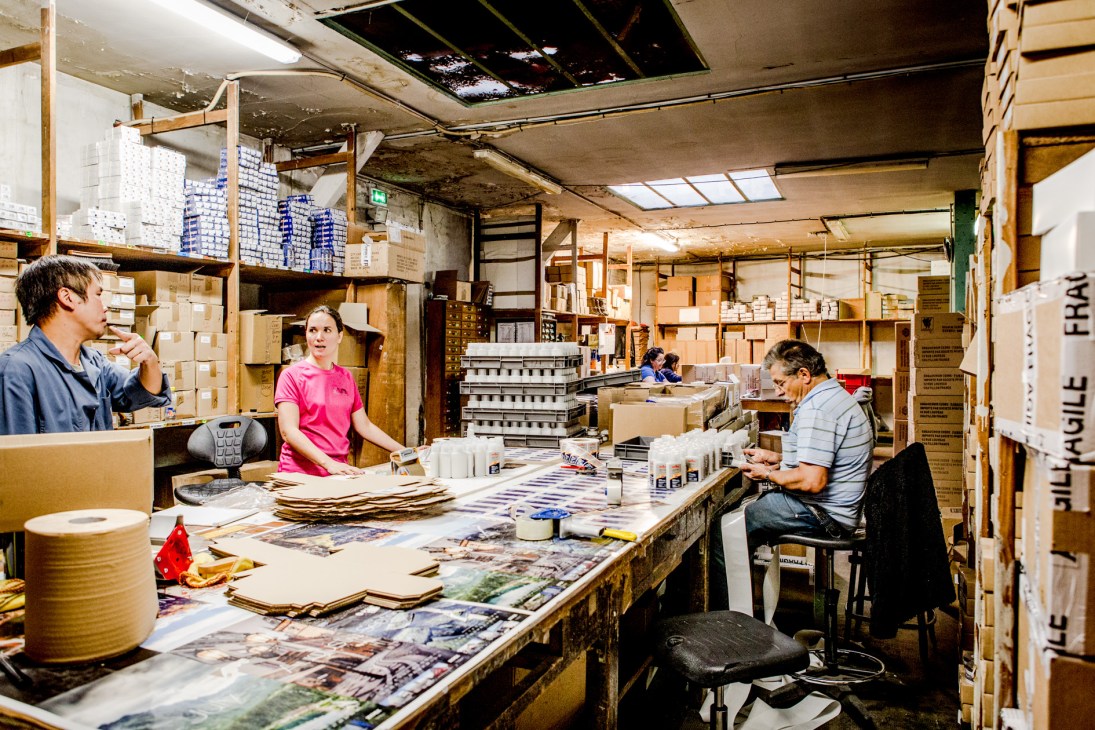 Famaco packaging area workers assembling products at a large table surrounded by cardboard boxes and shelving.