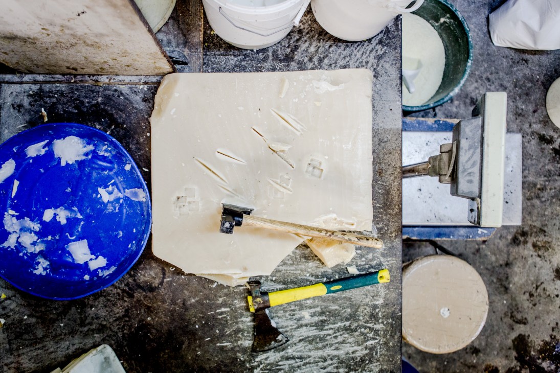 Large slab of pale beeswax with tools and containers on a work surface at Famaco factory.