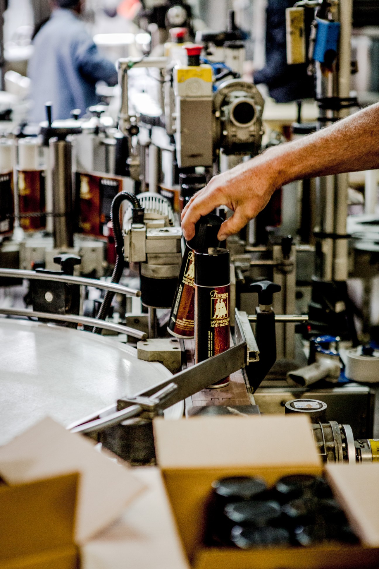 A worker's hand inspects a Famaco shoe polish bottle on a factory production line.