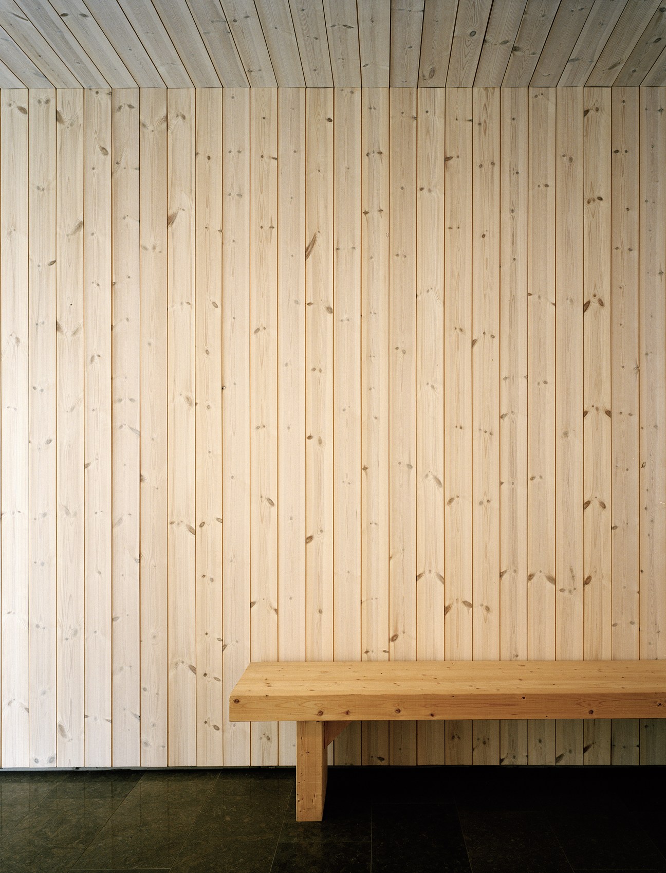 Wood-clad interior wall and bench in a lobby with light pine paneling.