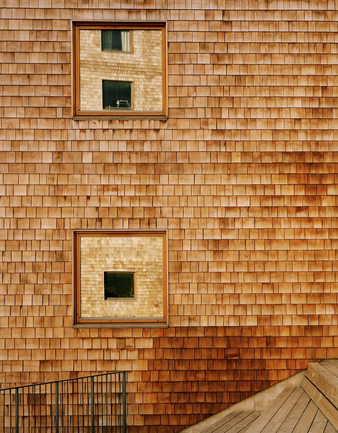 Cedar wood shingle facade of Strandparken building with two square windows and wooden deck railing.