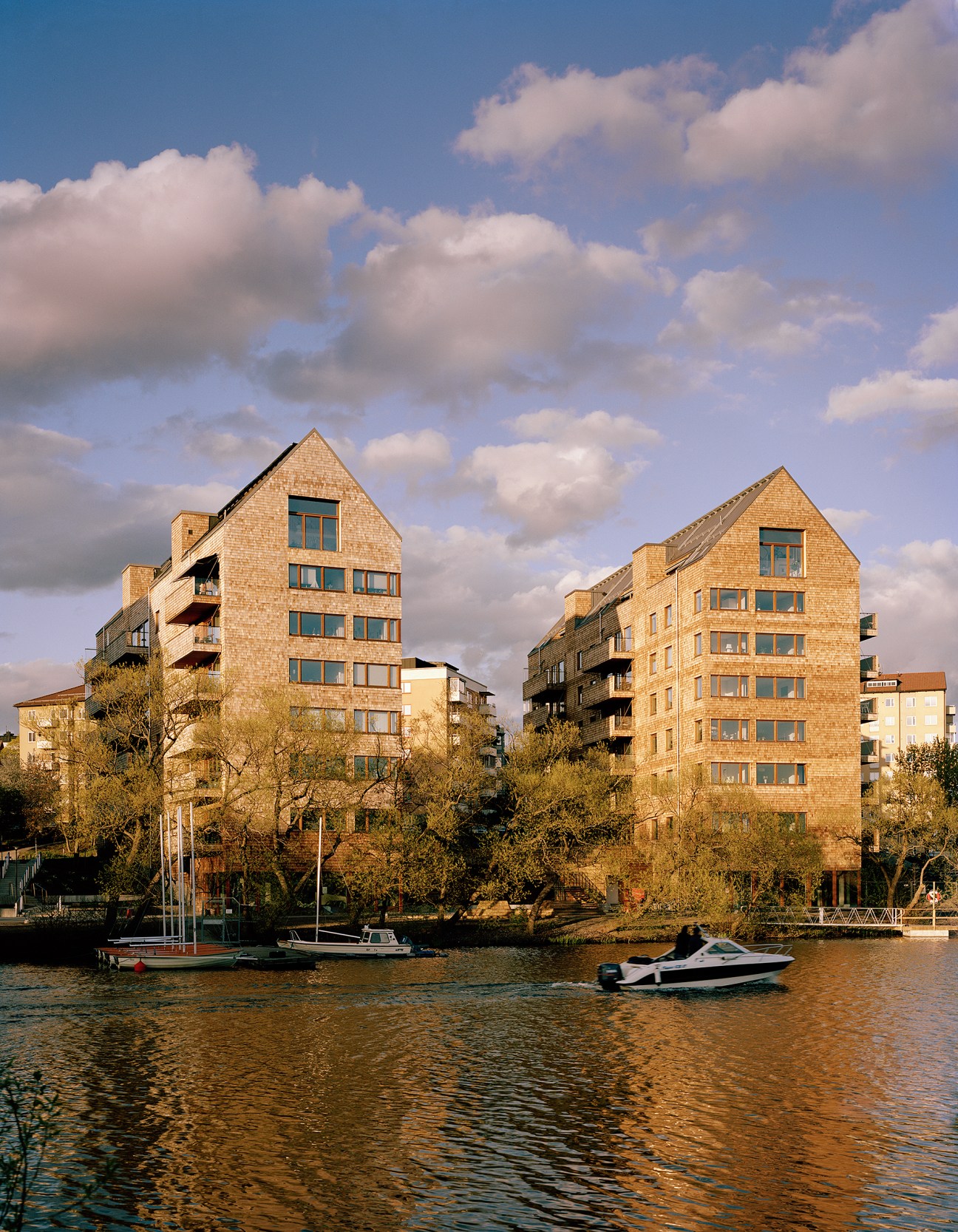 Wooden apartment buildings on the waterfront with boats docked in the foreground.