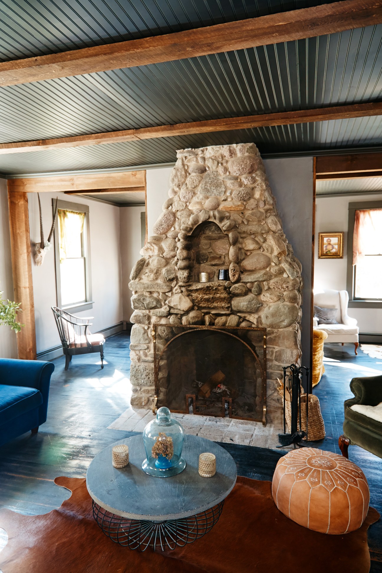 Stone fireplace with metal fire screen in modern rustic interior with exposed beam ceiling.