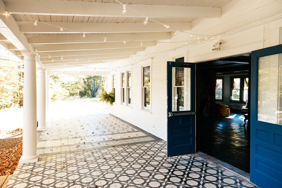 Modern covered patio with white columns, blue doors, geometric patterned flooring, and track lighting at Foxfire Mountain House.