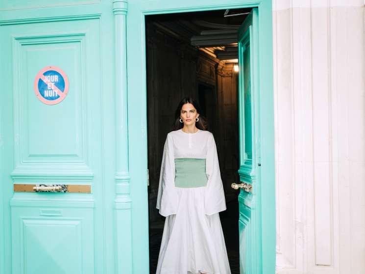 Woman in white Loewe dress with green square detail standing in turquoise doorway in Paris