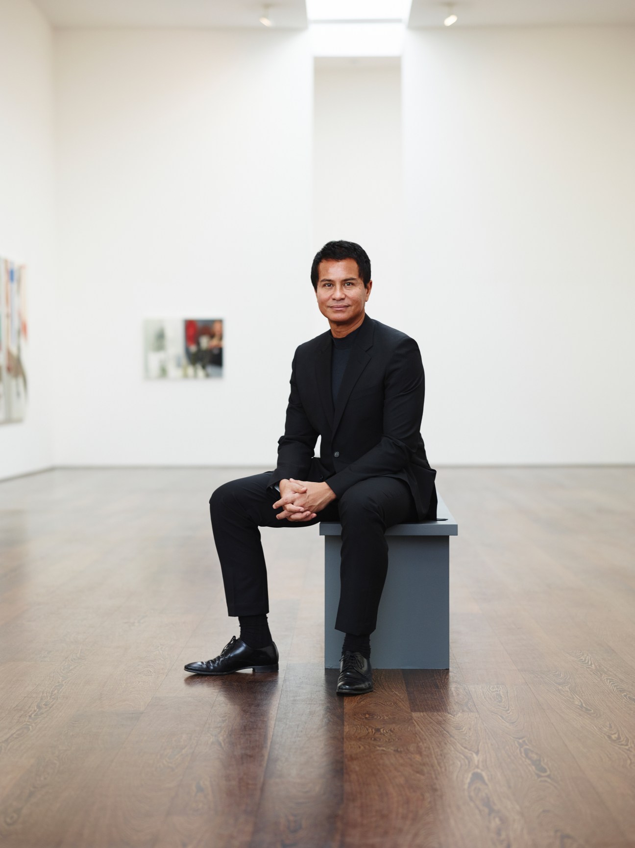 Glenn Scott Wright, director of Victoria Miro gallery, sits in a minimalist white gallery space with artworks on the walls.