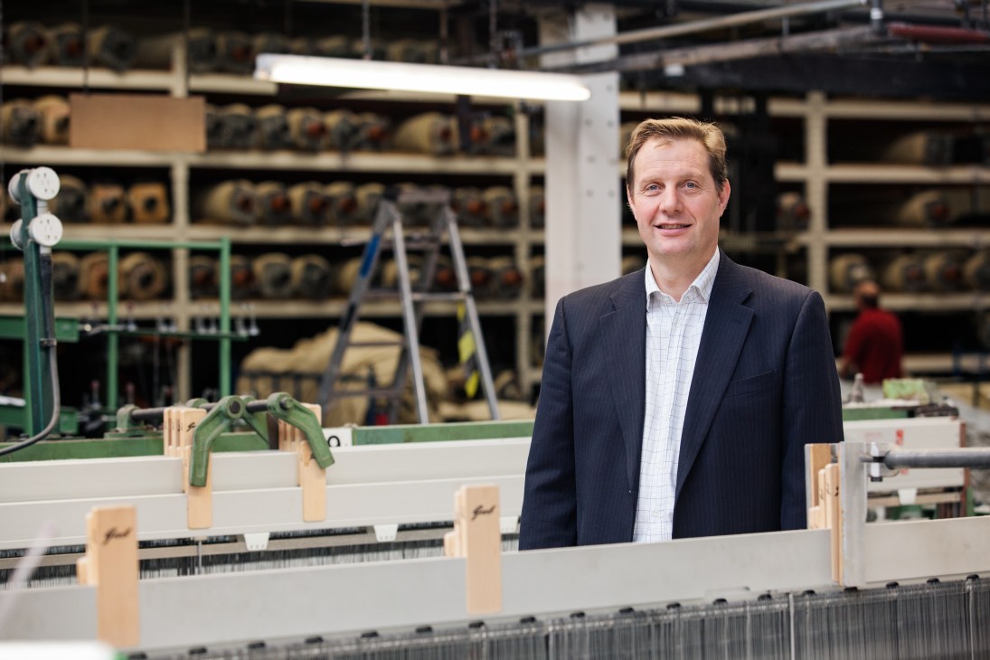 Man in business casual attire standing at textile machinery in a factory setting.