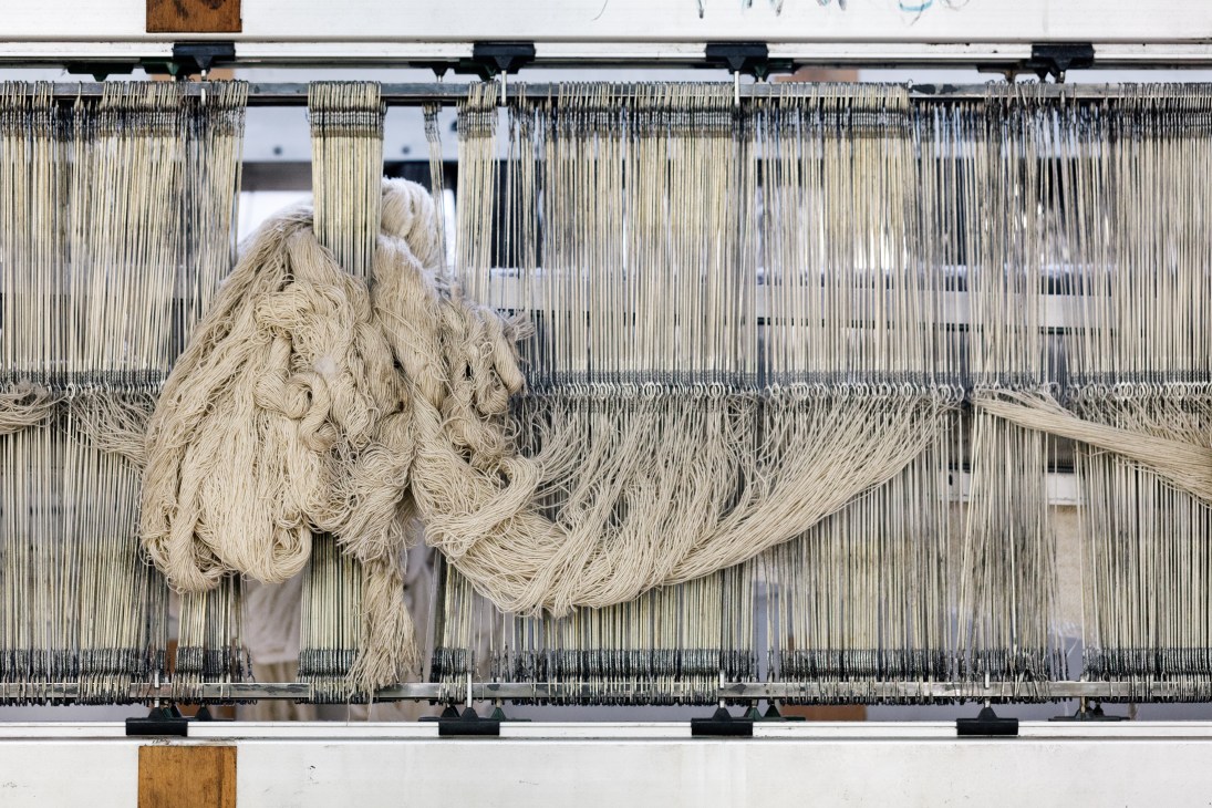 Cream-colored wool yarn hanging on weaving loom mechanisms at Hainsworth mill.