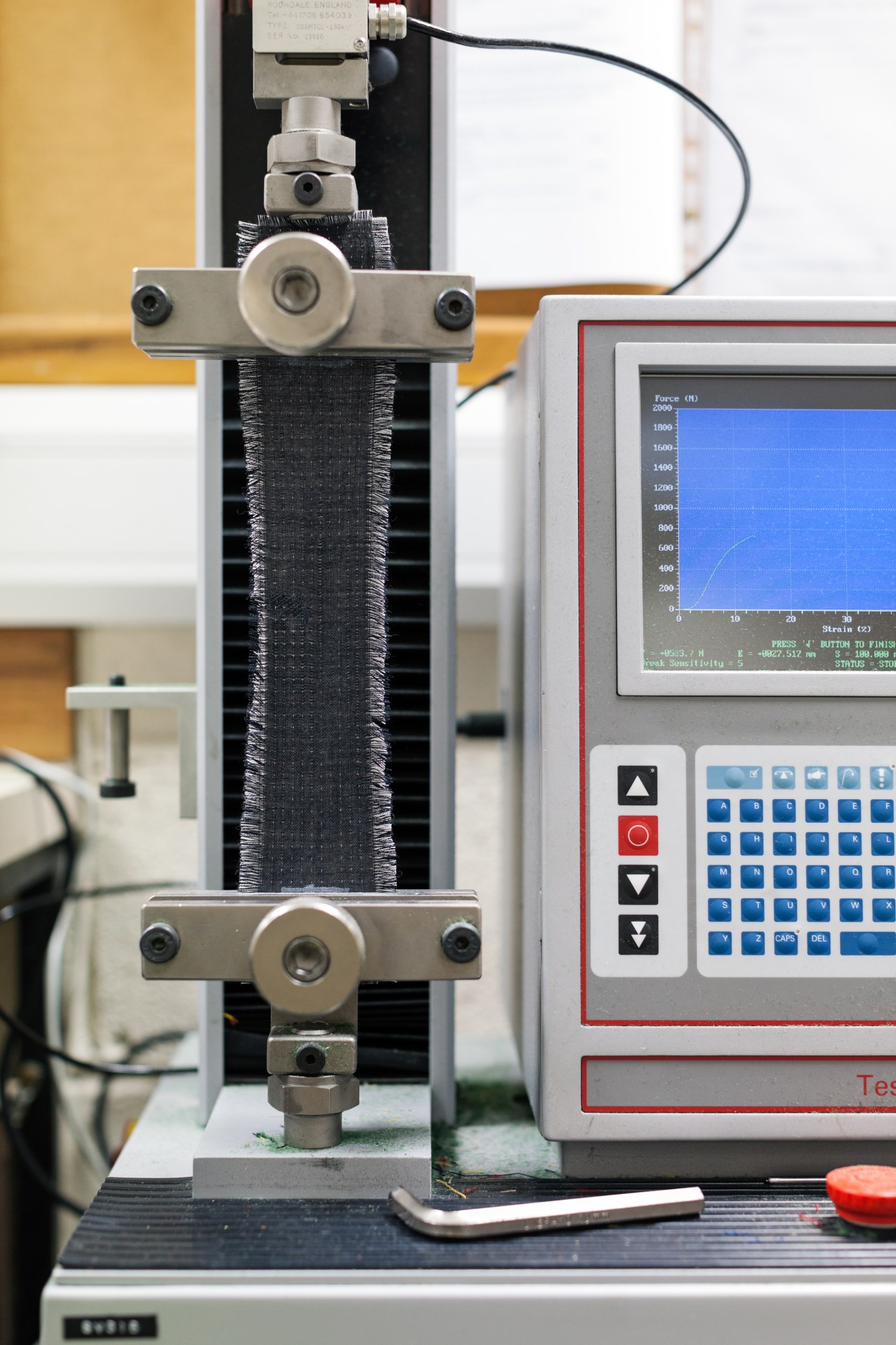 Fabric sample held in tensile testing machine with force measurement display.