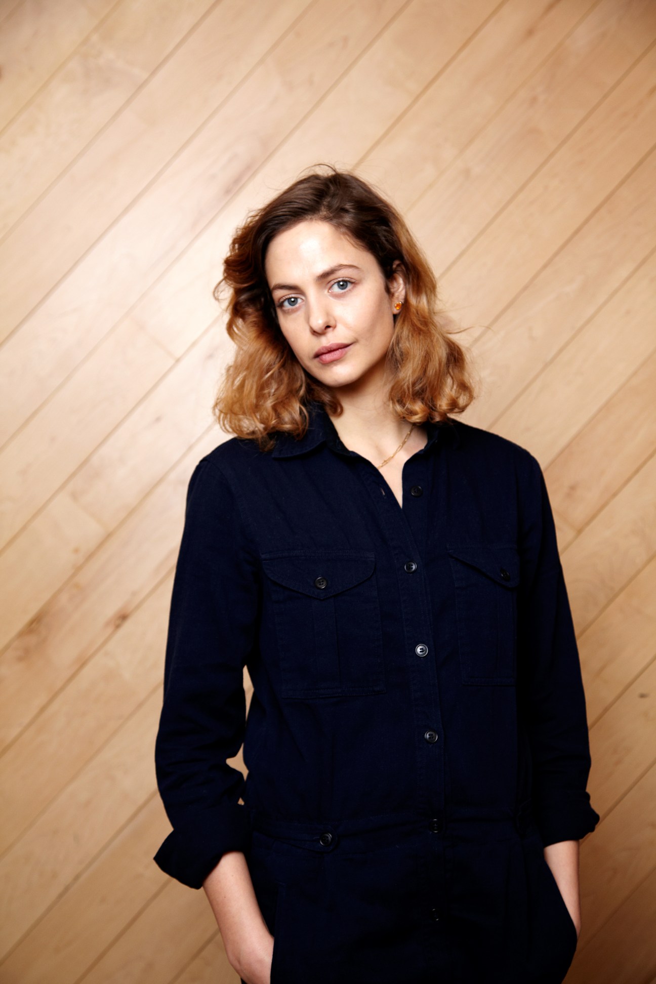 Musician Hannah Cohen wearing a dark navy button-up shirt against a wooden wall backdrop.