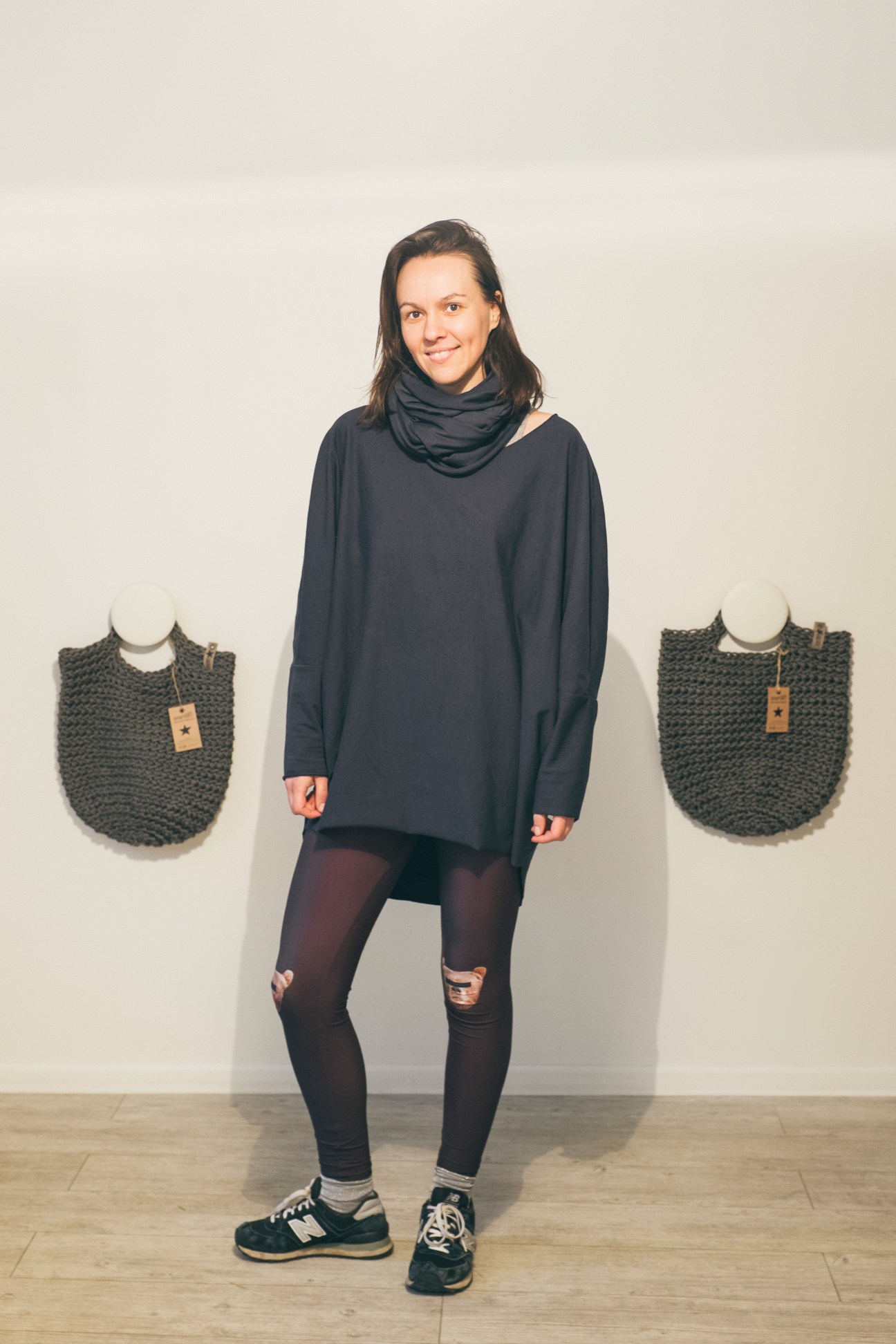 Designer Justina Skurdelyte poses with handwoven bags displayed on mannequins behind her.