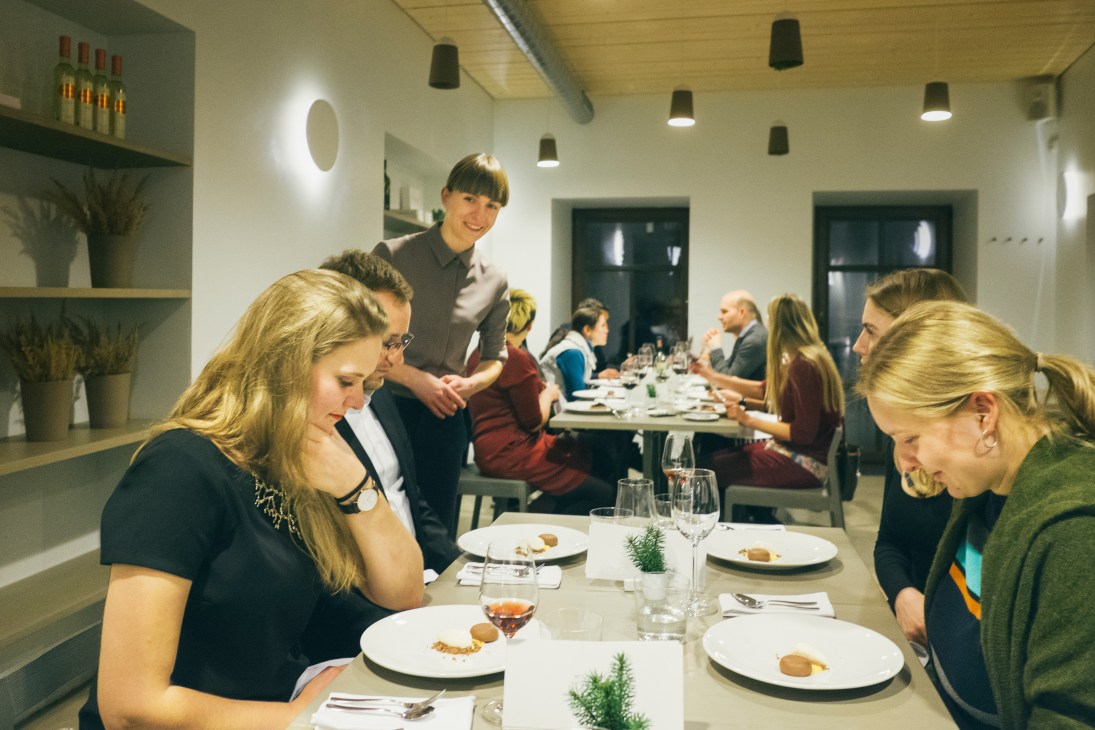 Diners enjoy a meal at a modern restaurant with minimalist white interior and pendant lighting.