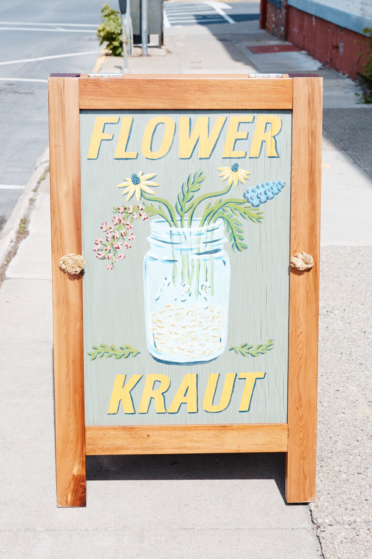 Wooden sign for Flowerkraut with painted jar and flowers illustration on Warren Street, Hudson.
