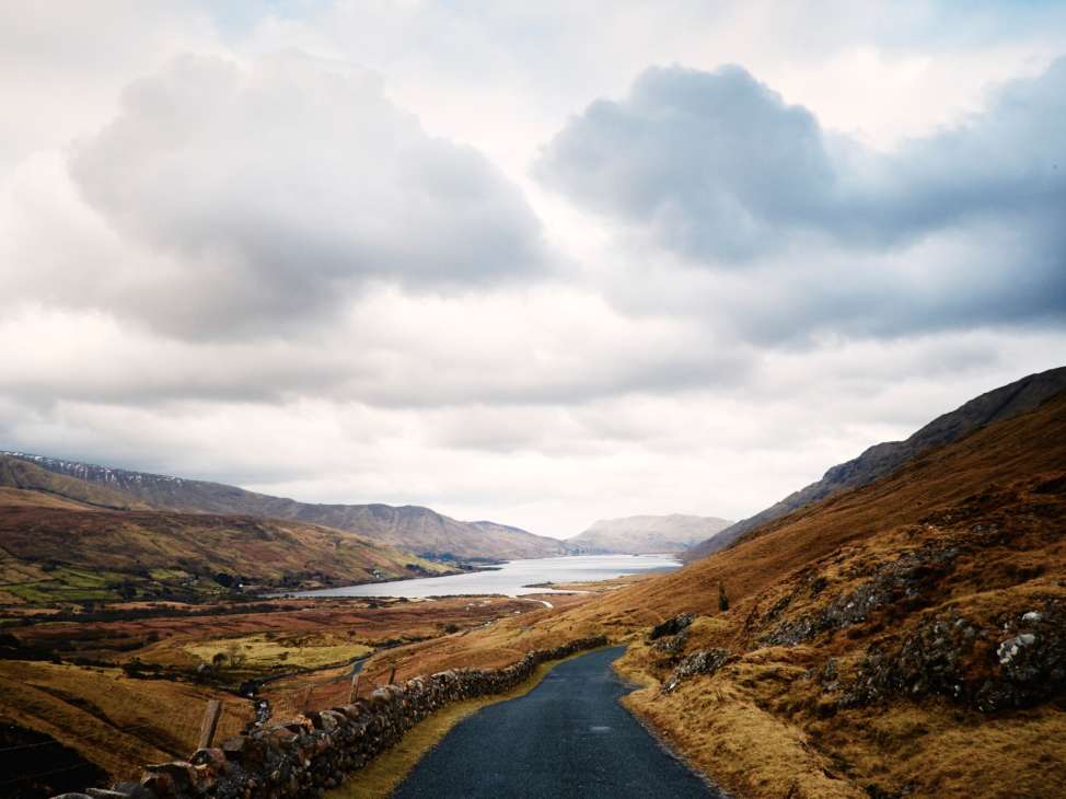 Scenic Irish landscape with mountains, a lake, and winding road under cloudy skies