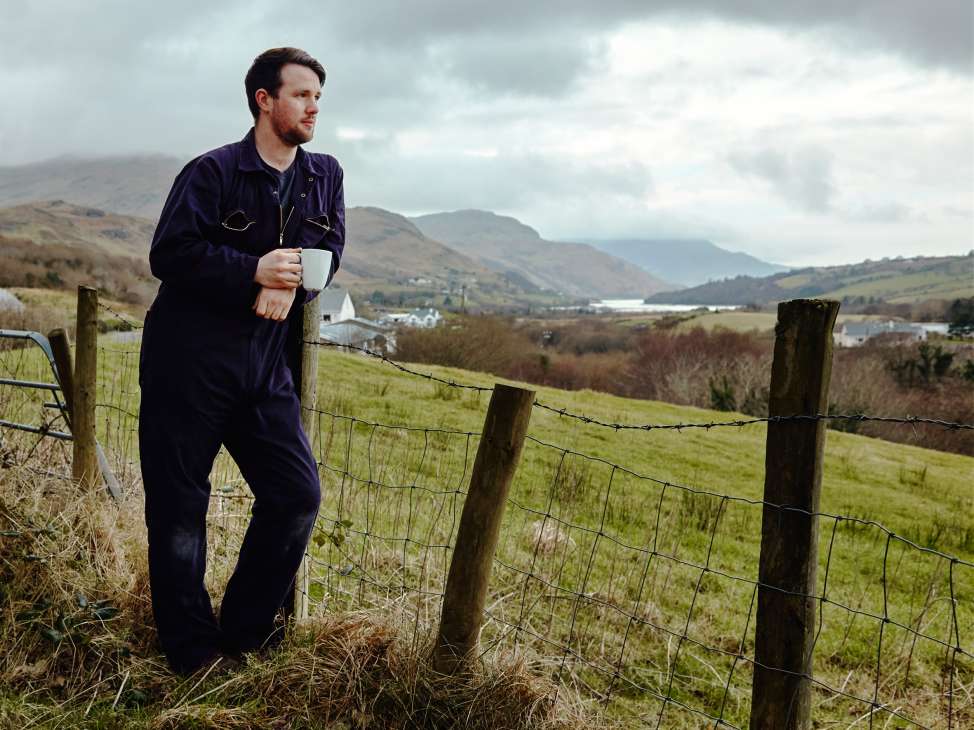 Kieran Molloy, director of Molloy & Sons, stands in a Donegal hillside landscape holding a mug.