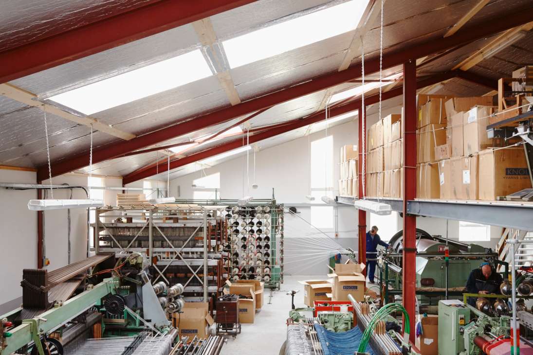 Interior of Molloy & Sons textile factory floor with looms and machinery under red beam ceiling.