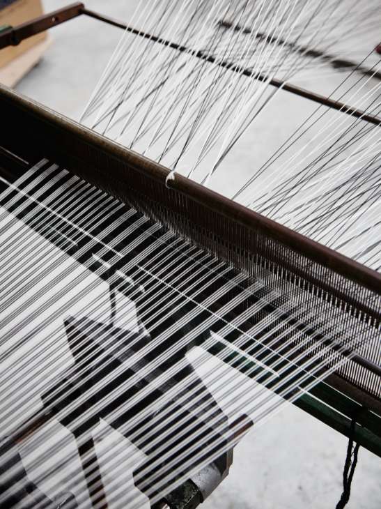 Close-up of a weaving loom with white threads creating a Prince of Wales check pattern at Molloy & Sons.
