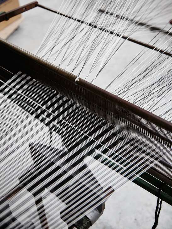 Close-up of a weaving loom with white threads creating a Prince of Wales check pattern at Molloy & Sons.