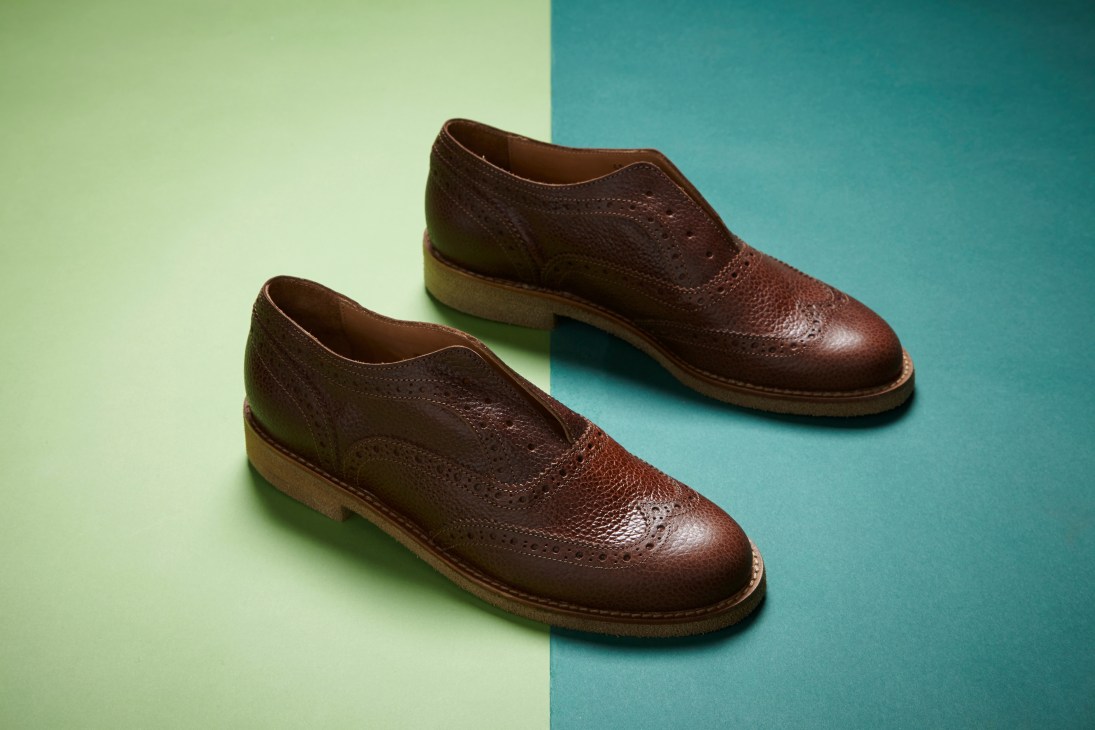 Pair of brown leather slip-on brogues by L'F Unisex with no shoelaces or tongue on a split green and teal background.