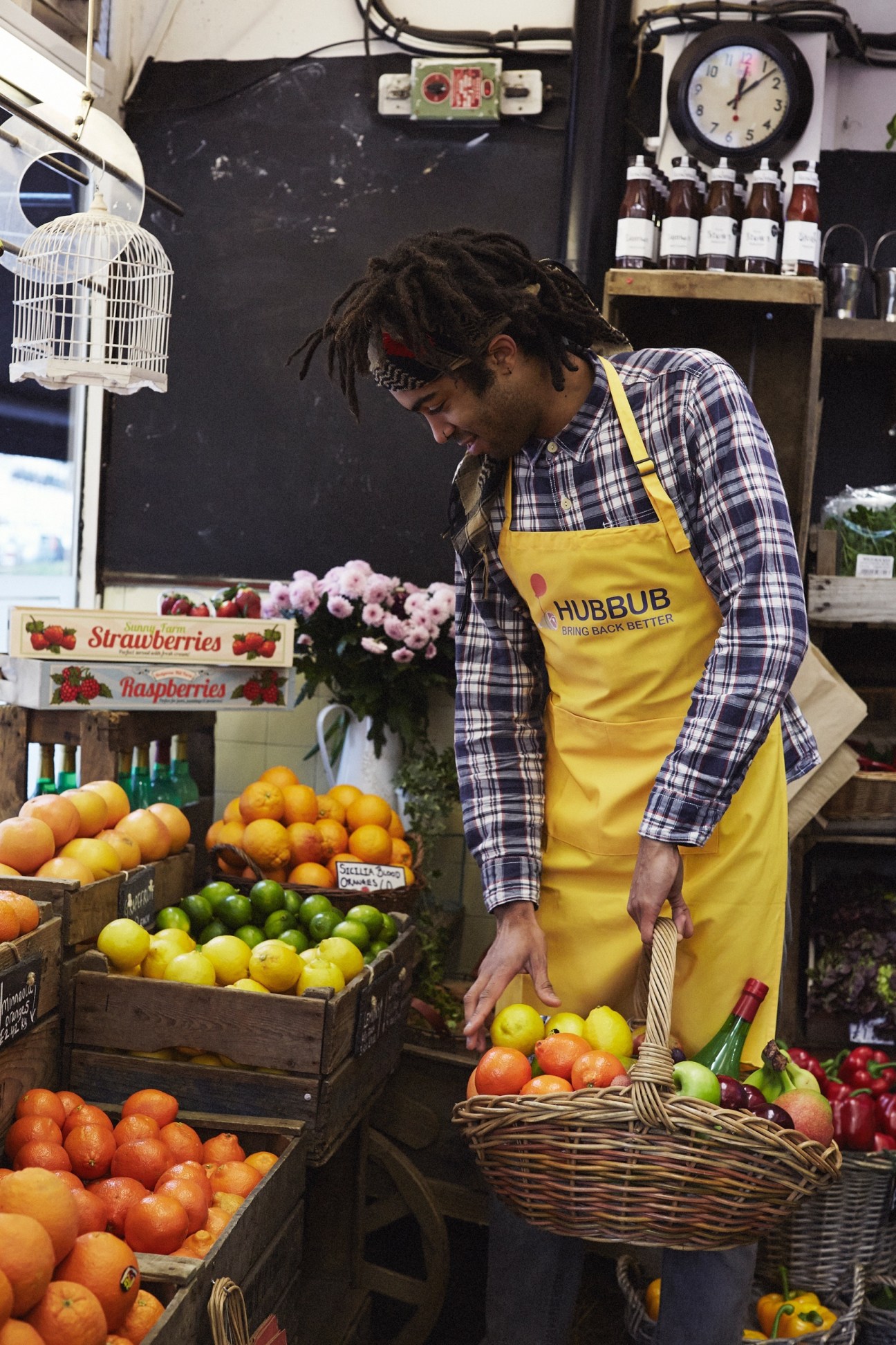 Hubbub delivery worker in yellow apron selecting fresh fruit at a local produce market.