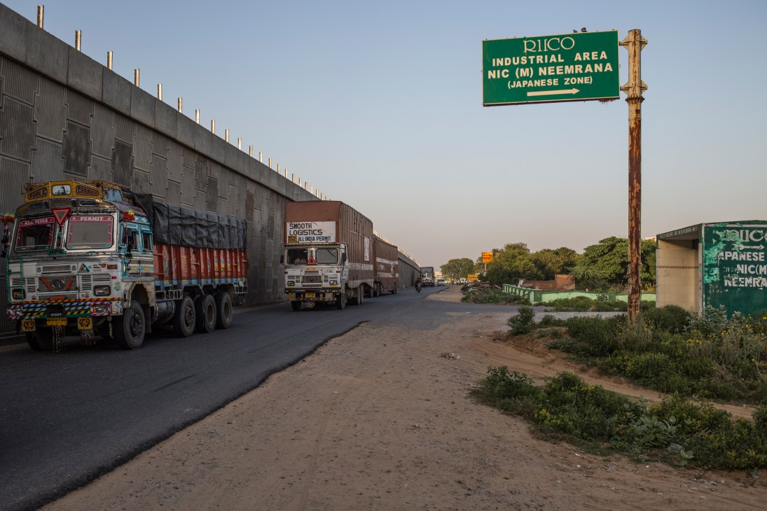 Sign marking entrance to RIICO Industrial Area NIC (M) Neemrana Japanese Zone with Indian trucks parked nearby