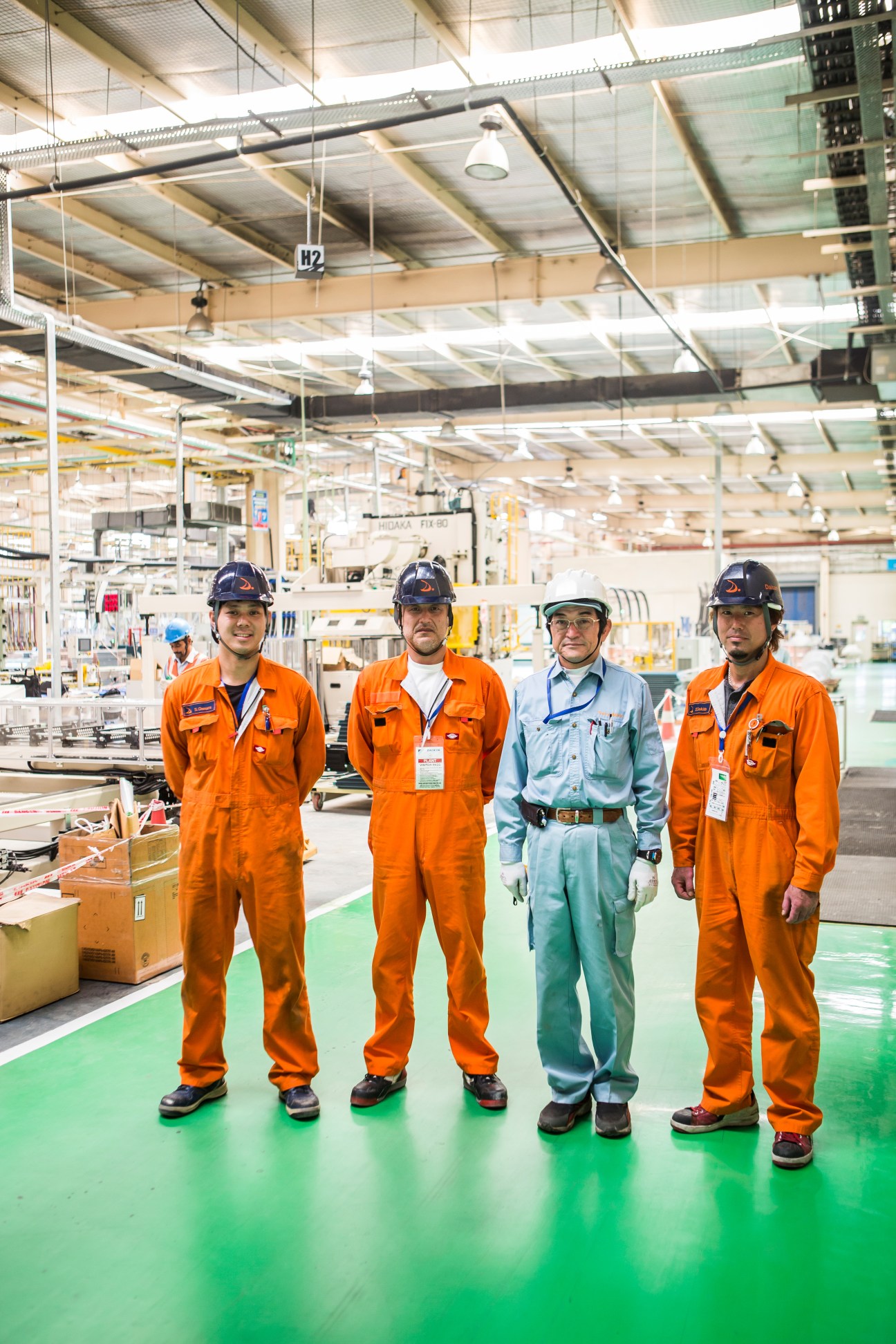 Four technicians in safety helmets stand on a factory floor at the Daikin factory in Neemrana, three wearing orange uniforms and one in green.