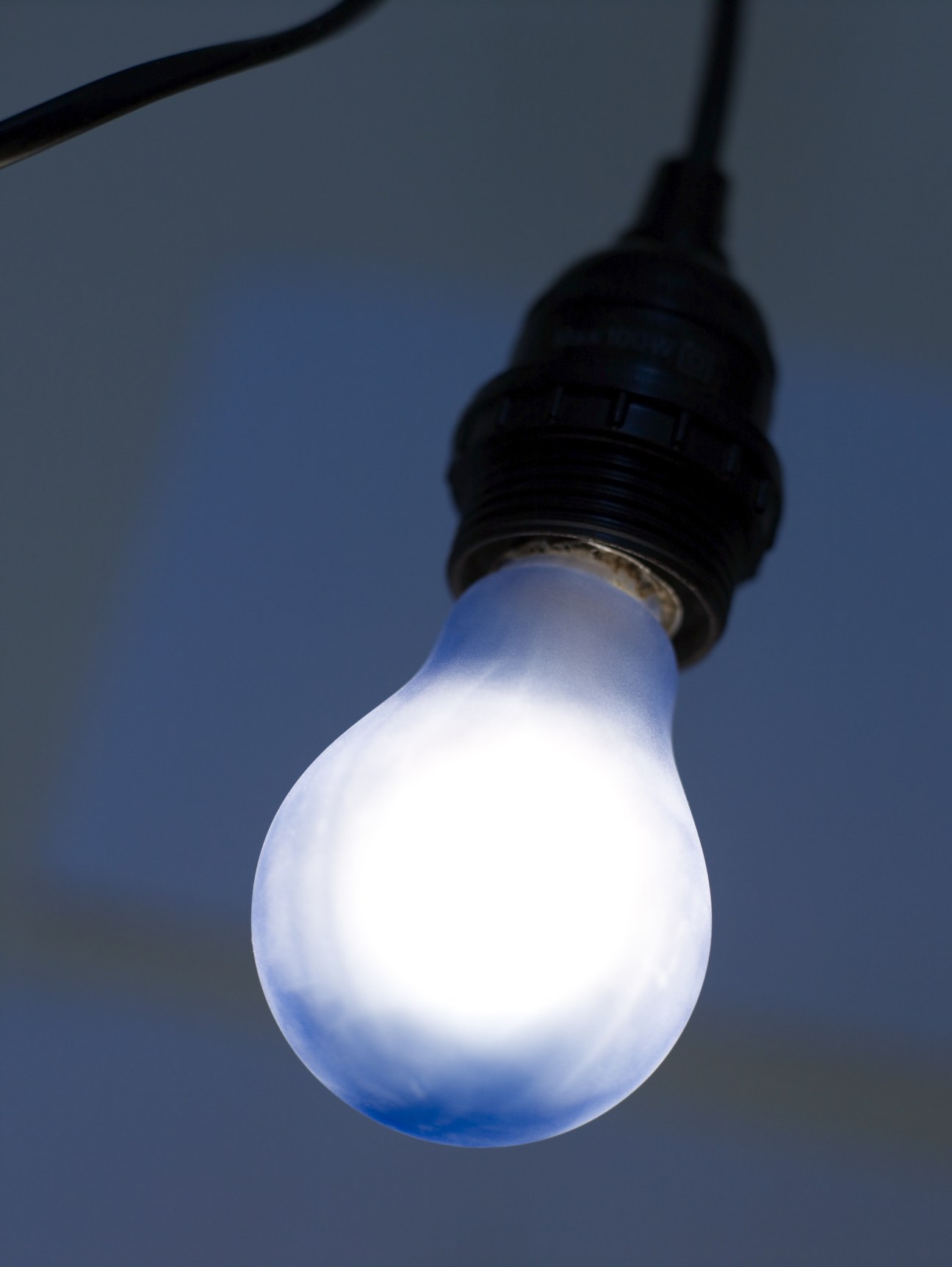 A glowing light bulb with a blue-white moonlight-tinted glow hanging from a black cord against a twilight background.