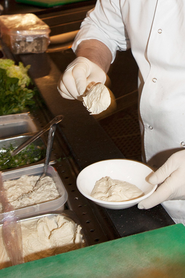 Chef in white gloves serving hummus from a bowl at Maroush Gardens restaurant.