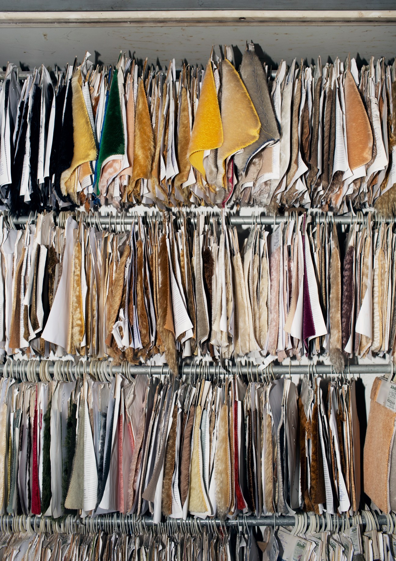 Fabric swatches in various colors and textures hanging on rods in an organized archive system.