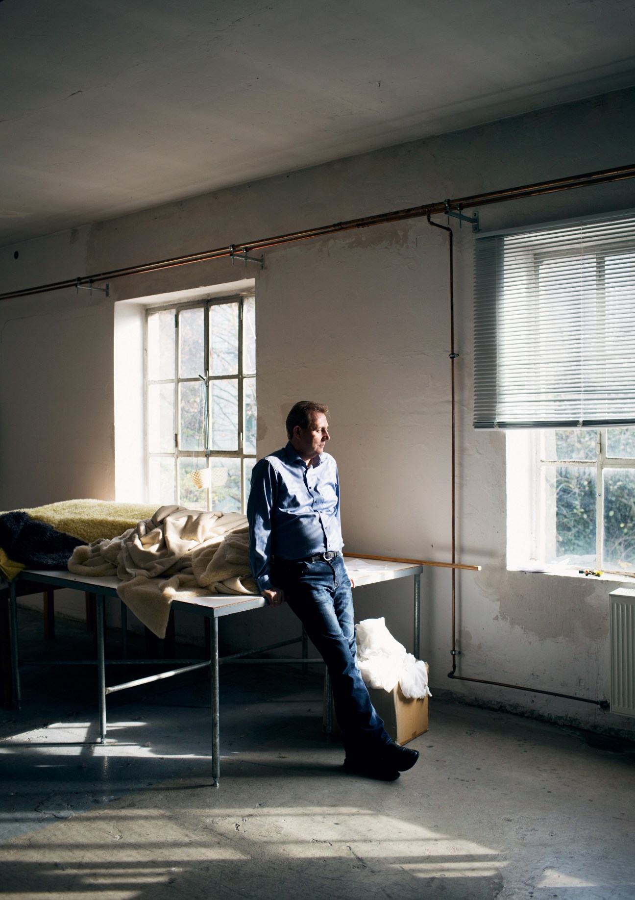 Bernhard Wanning stands in a factory room beside fabric samples on a table.