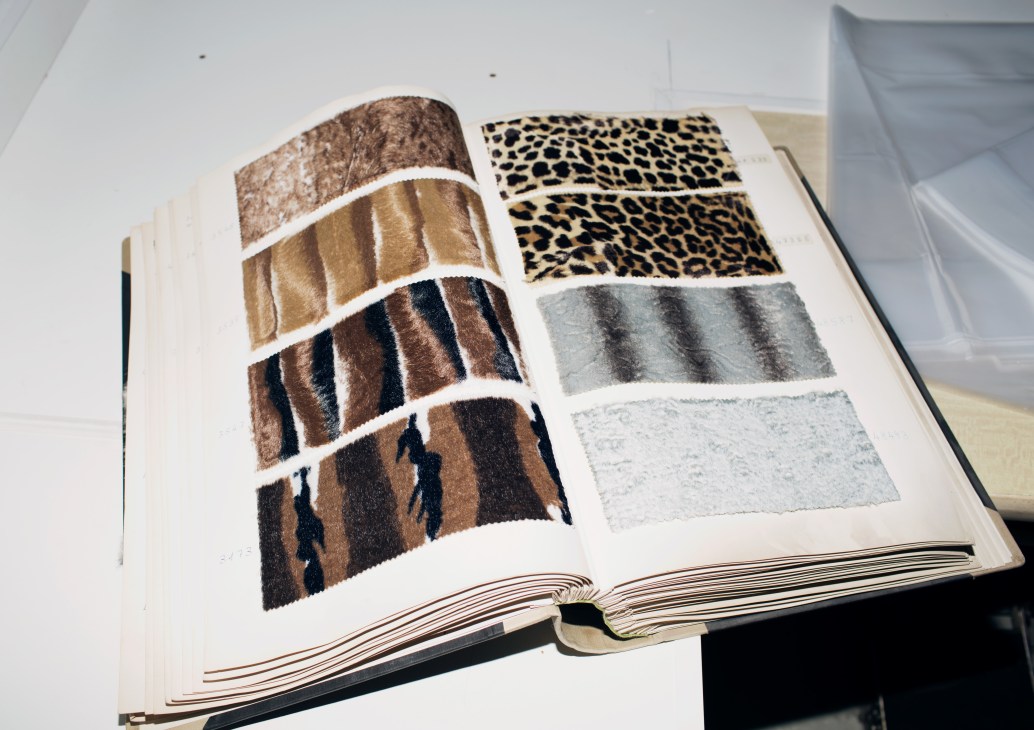 Open fabric sample book displaying various artificial fur textures and patterns in brown, tan, leopard print, grey and white.