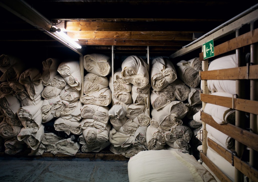 Rolled and stacked light-colored fabrics organized in storage racks within an industrial stockroom.
