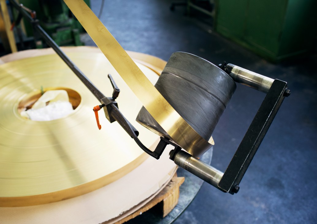Brass metal rings in pre-popper state wound on industrial machinery during Prym button manufacturing.