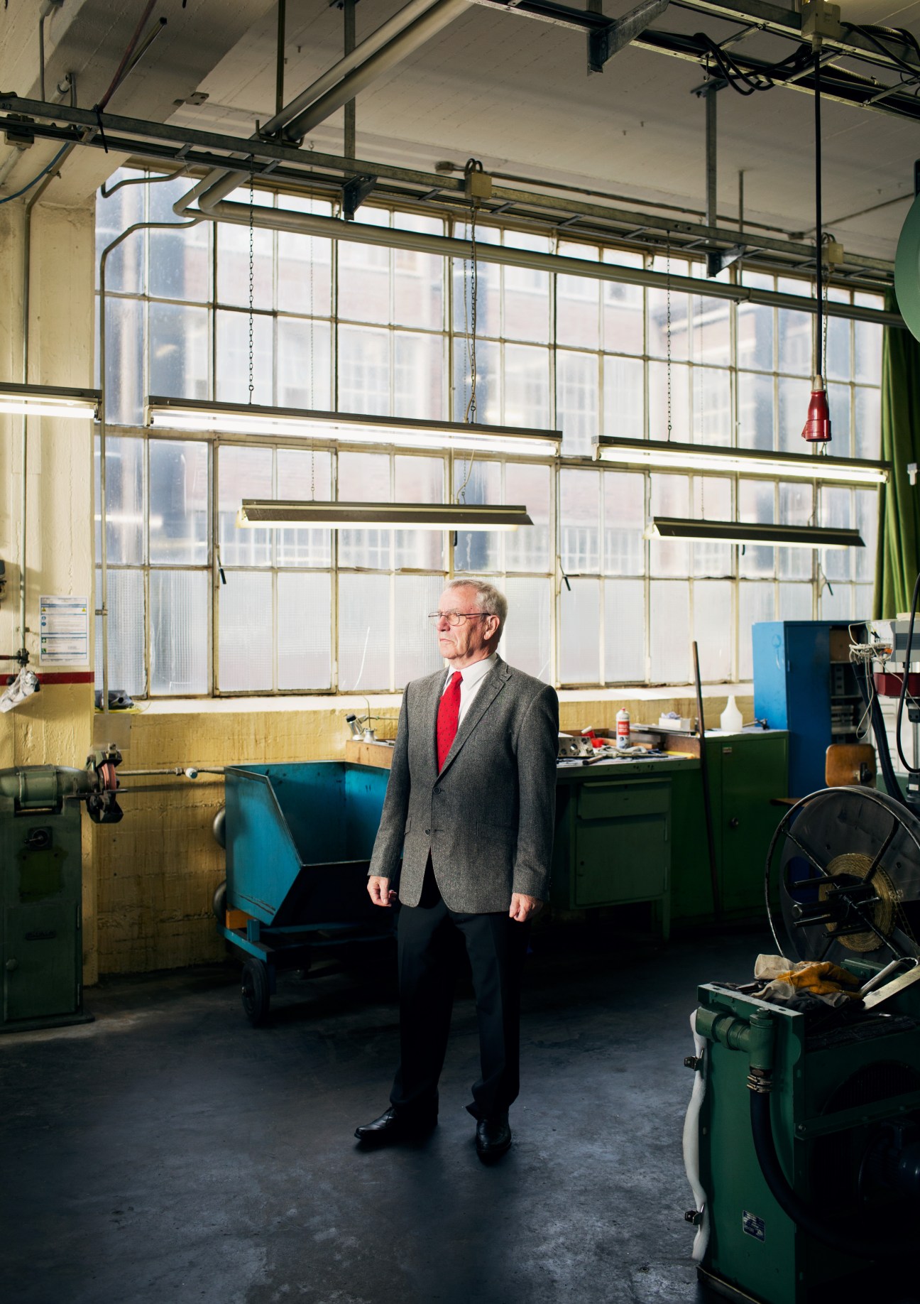 Rudolf Malmendier, a retired Prym employee of 45 years, stands in an industrial factory setting with large windows.
