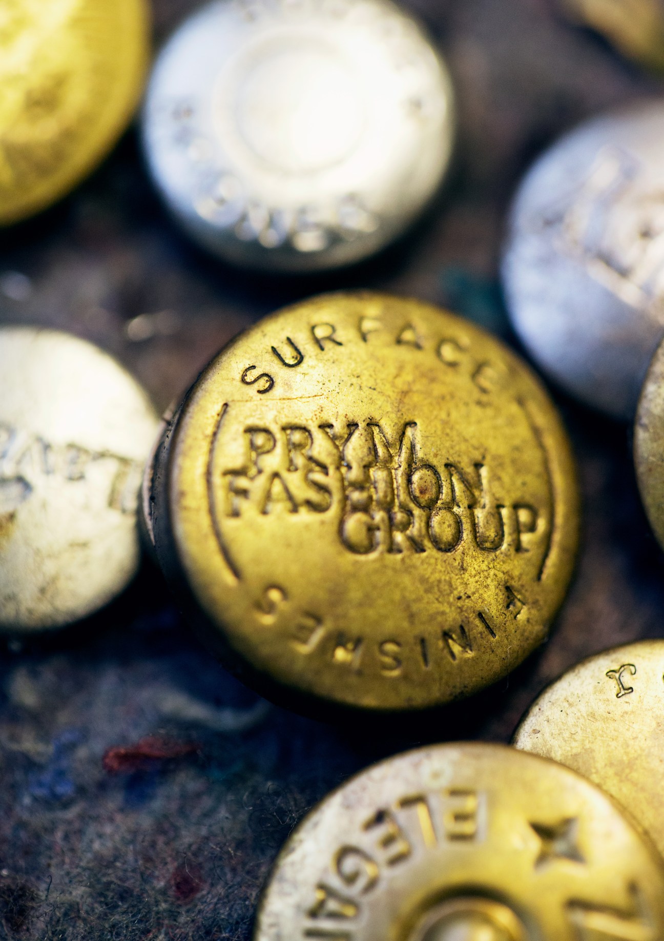 Close-up of Prym snap buttons with engraved text and logos in yellow and metallic finishes.