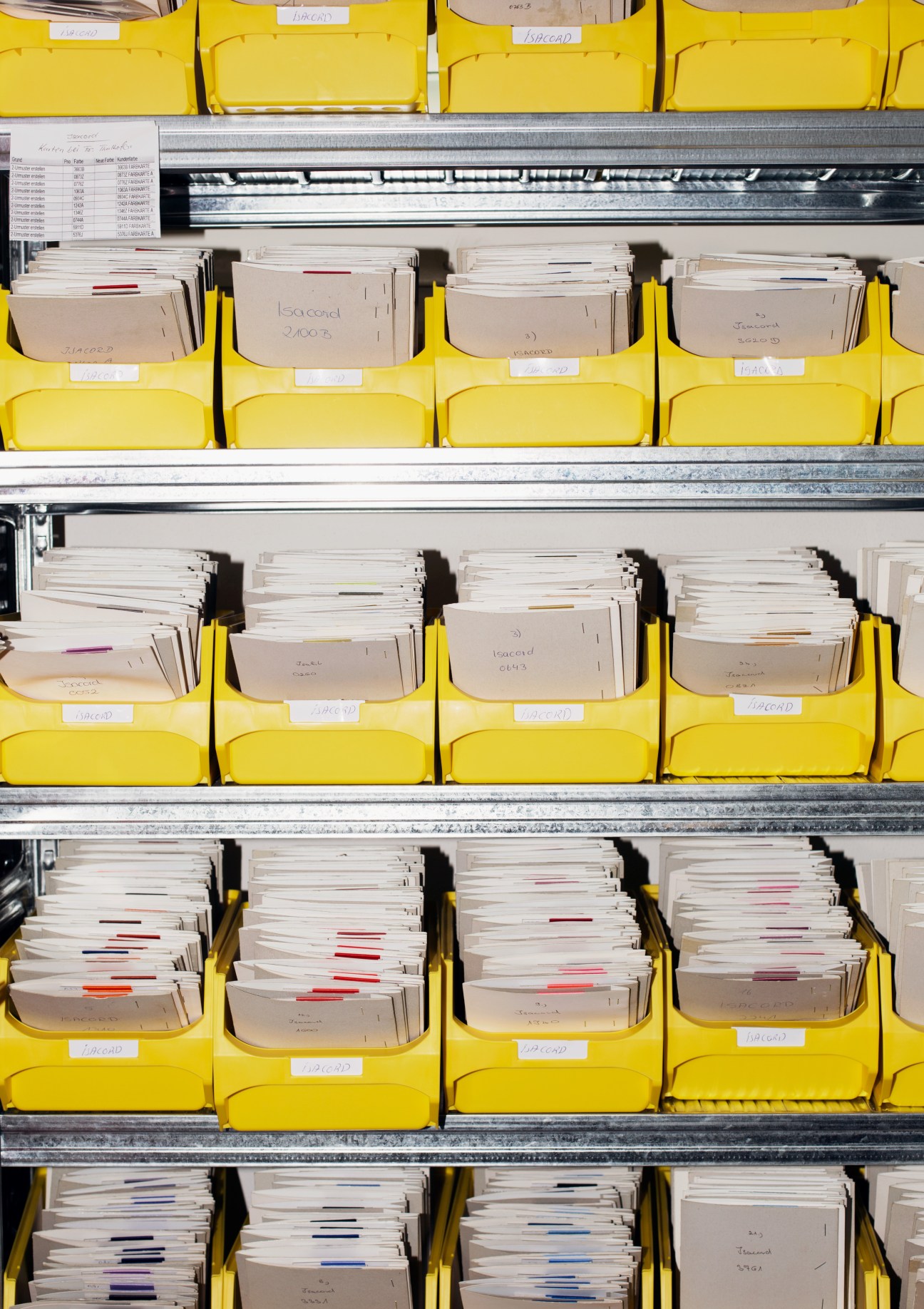 Yellow storage bins with fabric samples organized on metal shelving at Amann & Söhne's factory.