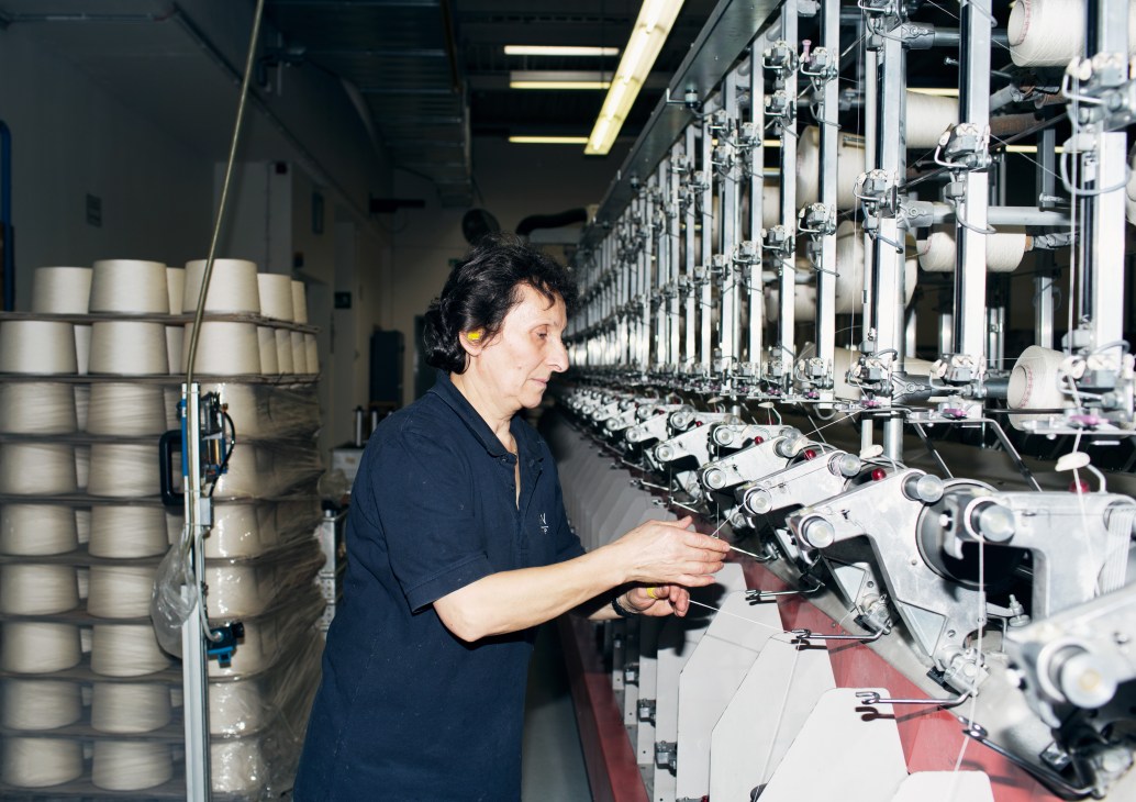 Female employee inspecting thread on spinning machinery in an industrial textile factory.