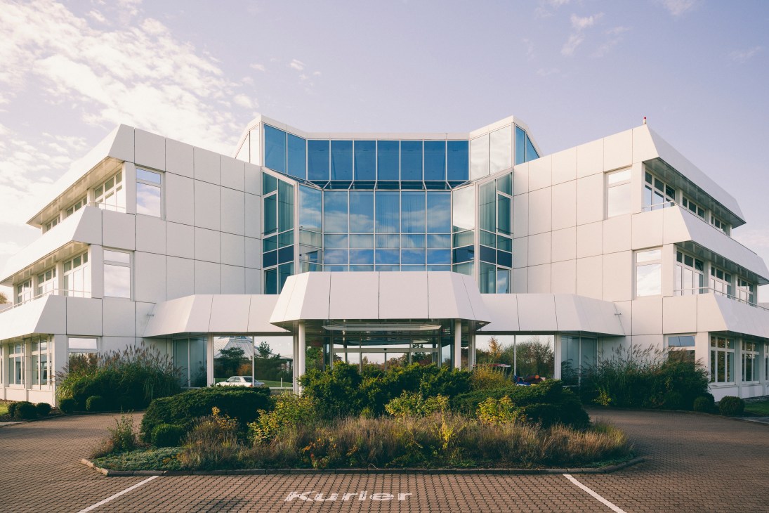 Modern white building with large glass windows and landscaped grounds at Playmobil headquarters in Zirndorf, Bavaria.